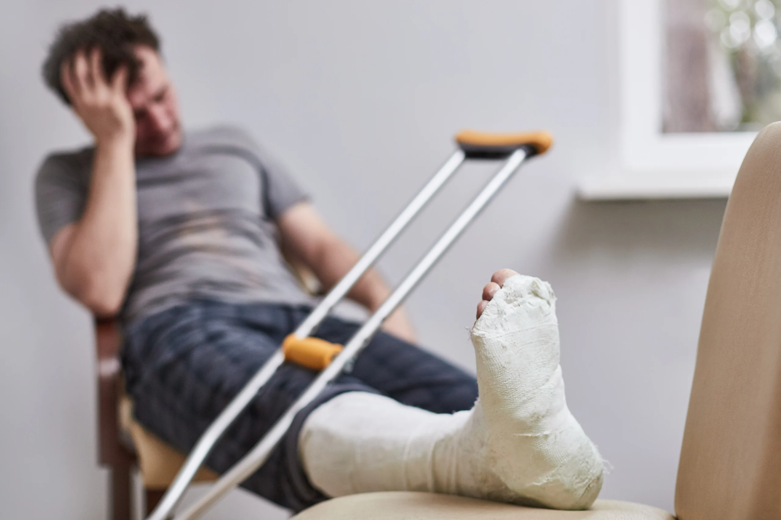 Seated man covering his head with a cast and crutches Seated man covering his head with a cast and crutches