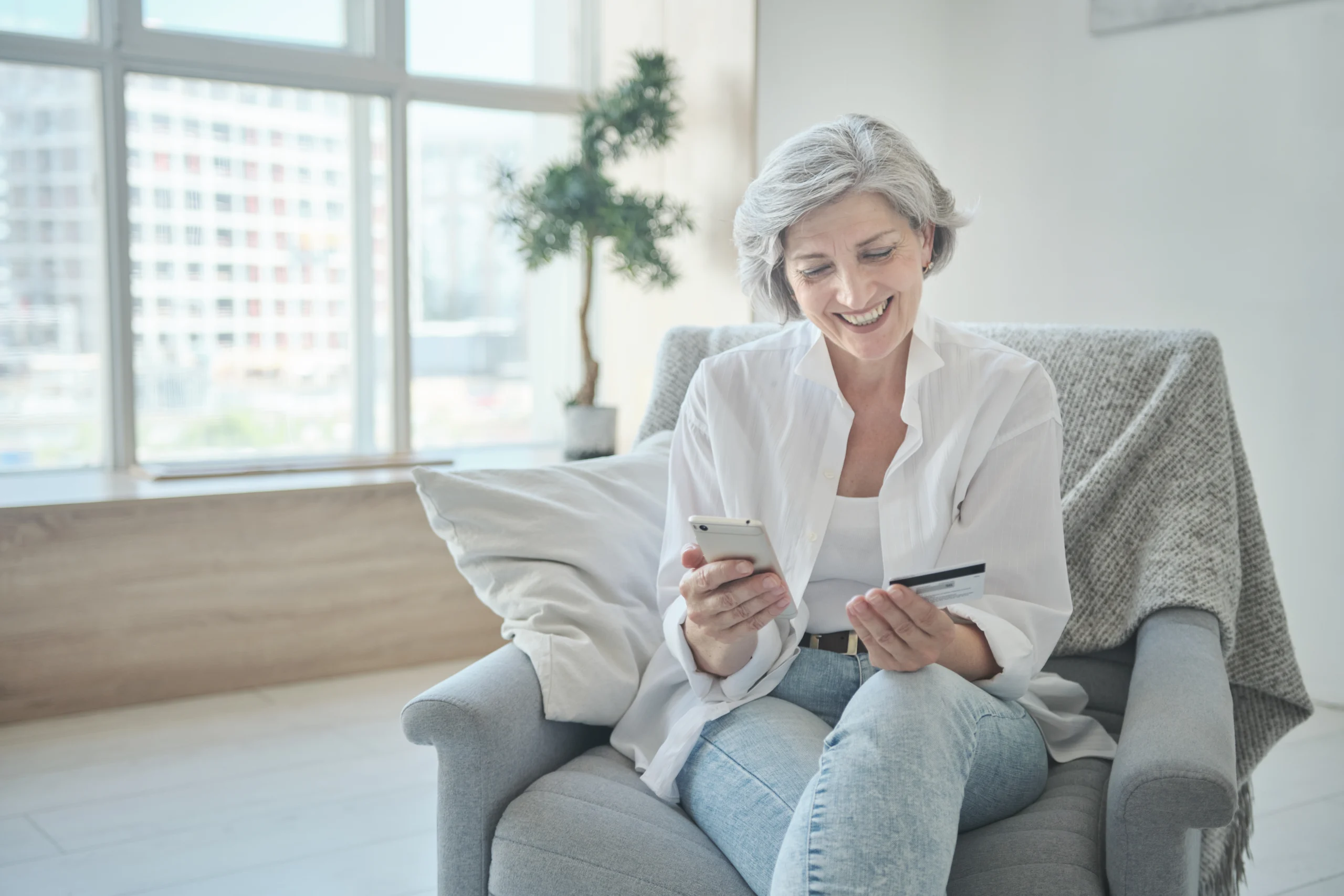 Seated senior female looking at phone and card in hand