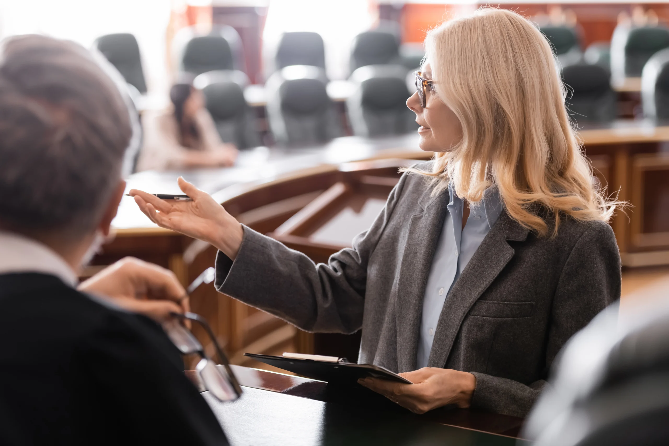 Professional female attorney pointing with hand near grey-haired judge in courtroom Professional female attorney pointing with hand near grey-haired judge in courtroom