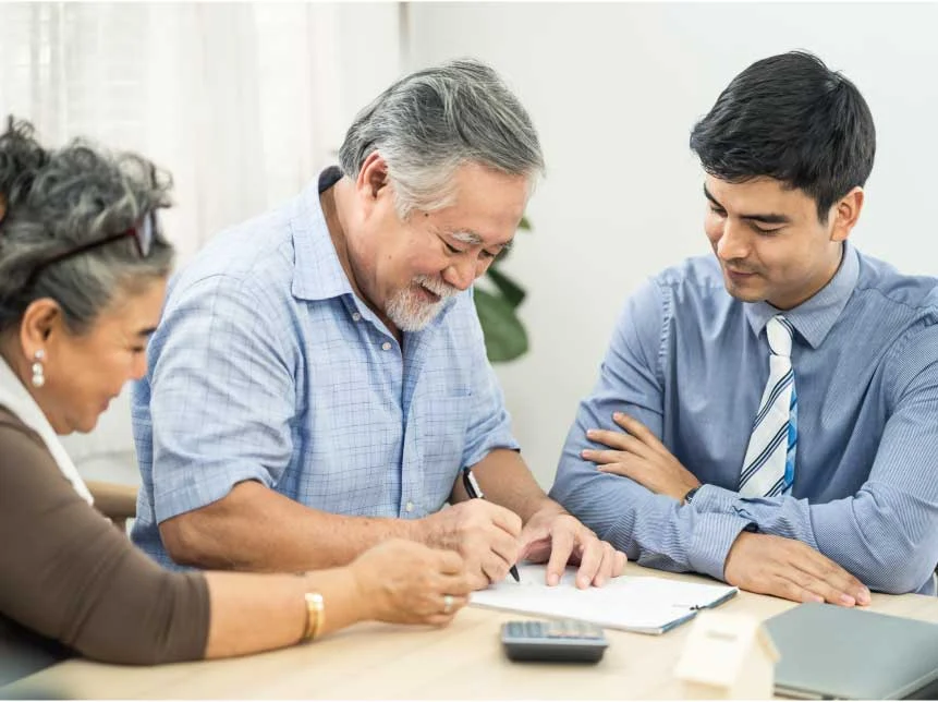 Happy senior couple seated with agent while reviewing information on desk Happy senior couple seated with agent while reviewing information on desk