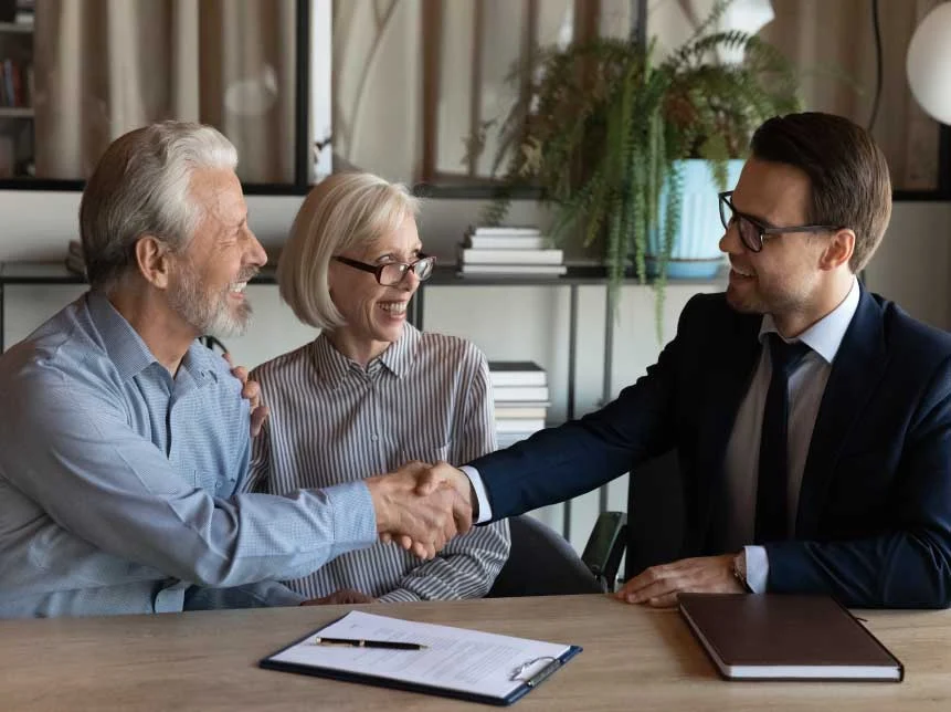 Smiling broker handshaking with senior couple.