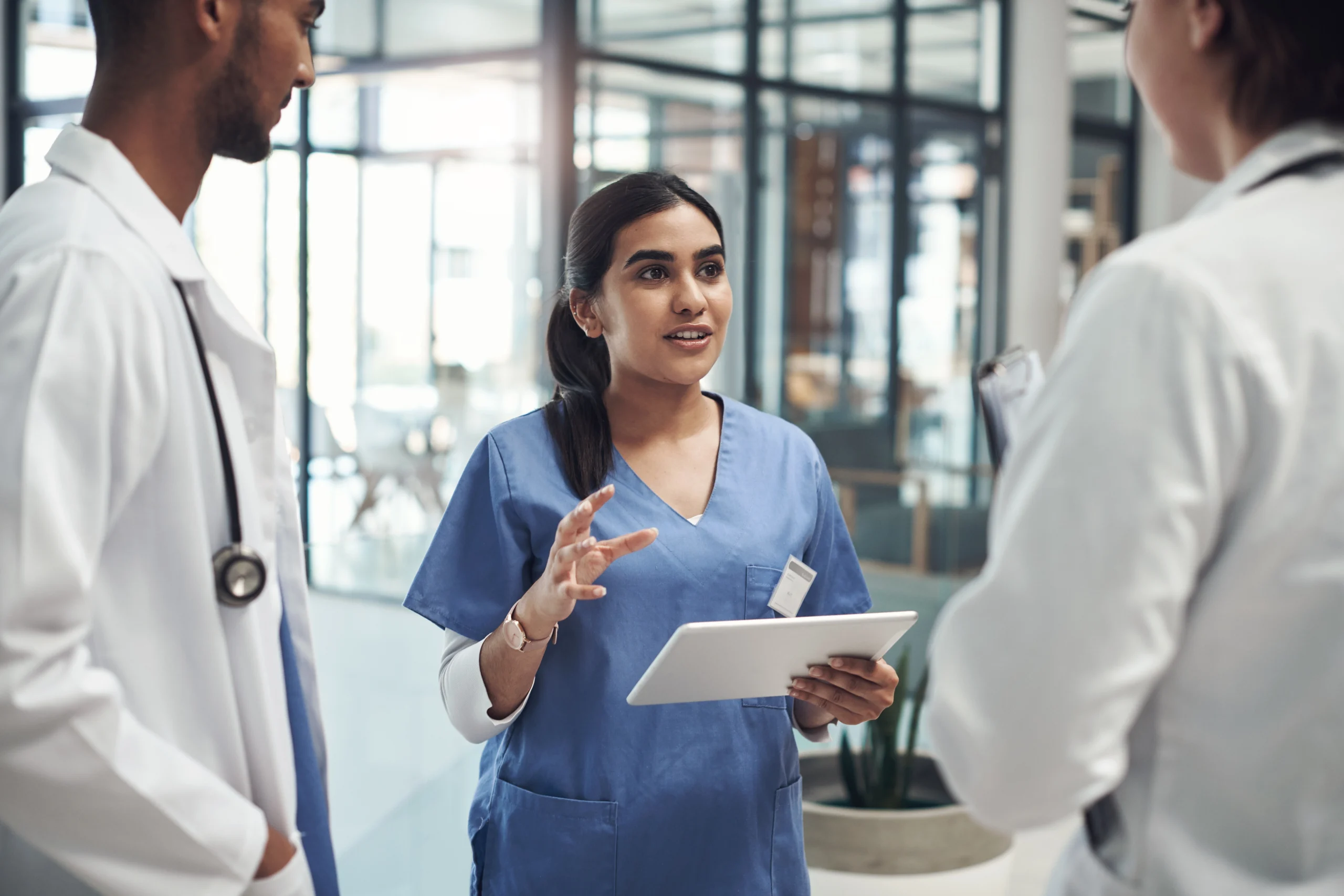 -female-nurse-in-blue-scrubs-holding-a-digital-tablet-and-talking-to-doctors-in-a-hospital-